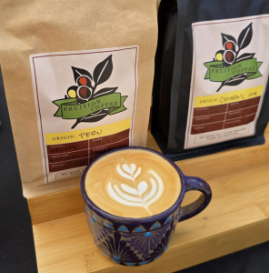 Bags of featured coffee beans with Fruition logo frame a mug with fresh latte art.