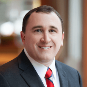Photo of man in dark grey business suit smiling at camera.