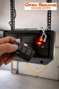Hand holding a wireless garage door opener remote syncing to an overhead opener unit with active red indicator lights.