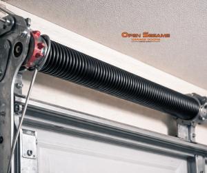 Close-up of a heavy-duty black garage door torsion spring and cable drum assembly installed overhead.