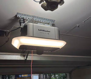 Ceiling-mounted LiftMaster smart garage door opener unit with illuminated LED light panel in a residential garage.