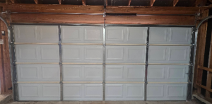 Interior view of a white multi-panel sectional garage door fully closed with torsion bar and track hardware.
