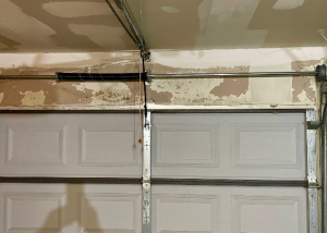 Overhead view of a black garage door torsion spring installed on a center torsion tube above a closed white door.