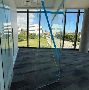 Modern commercial office interior featuring frameless glass wall partitions and floor-to-ceiling windows overlooking city views.