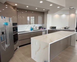 Modern kitchen renovation showcasing a white marble quartz waterfall island and seamless high-gloss taupe flat-panel cabinets.
