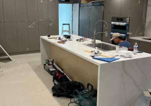 Construction phase of a kitchen remodel with a contractor installing a white waterfall island and modern cabinetry.