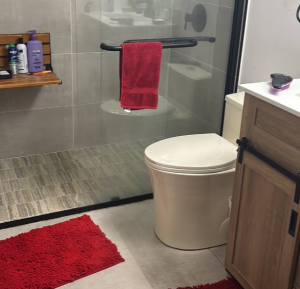 Renovated bathroom with a frameless walk-in glass shower, tiled shower floor, teak bench, and wood vanity.