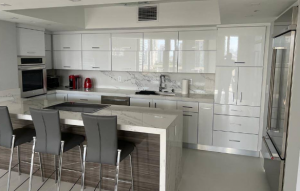 Sleek contemporary kitchen featuring high-gloss white upper cabinets, marble slab backsplash, built-in appliances, and breakfast bar with barstools.