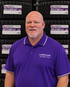 Chad Britton wearing a purple Landscape Durable Tires polo shirt in front of stacked tires.