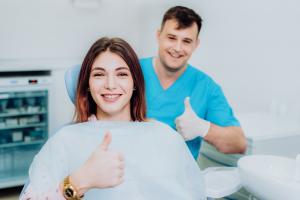 Smiling woman and dentist giving a thumbs up after successful cosmetic dentistry treatment