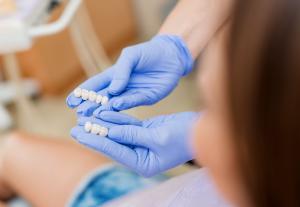 Dentist’s gloved hands holding a dental bridge and showing it to a patient
