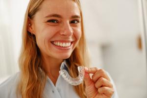 Woman smiling while holding her new Invisalign clear aligner