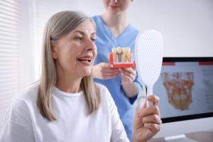 Woman looks at her reflection during a dental implant consultation as the dentist holds a dental implant model