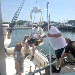 A man using the HandiCaptain boat boarding system is lowered from a dock into a boat while others assist.