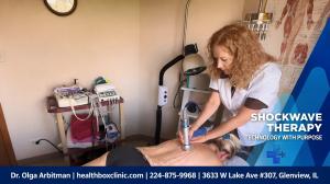 Licensed Doctor of Naprapathy Dr. Olga Arbitman performing shockwave therapy on patient's upper back with handheld device in treatment room at Health Box Clinic Glenview IL 60026.