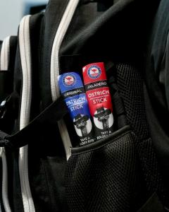 AOF Original and Jalapeño Ostrich & Premium Beef Snack Sticks tucked into a backpack pocket, highlighting their convenient, portable format for travel, work and outdoor adventures.