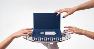 An open navy Everwow Physical Gift Box on a silver tray, with a gift card and QR code inside, as hands reach toward it.
