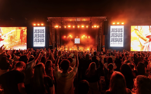 Large crowd with raised hands worshiping Jesus at the JESUS, JESUS, JESUS Easter Week 2026 gathering in Manvel, Texas, with a brightly lit stage and live Christian band.