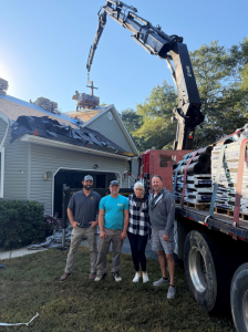 R. Short Roofing team members posing with giveaway recipient Christine Squires in front of a crane truck during her roof replacement.