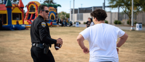 Police officer holds a football while speaking with a young man at an outdoor event with inflatable play structures.