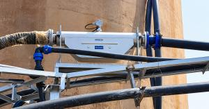 Silver Instruments Coriolis mass flow meter with flanged connections, mounted on a steel frame outdoors next to a large vessel