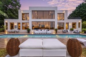 Twilight view of the staged pool deck at 1400 Aqua Vista Lane in Henrico, Virginia, with sculptural white loungers and resort-style furniture by Jsquared Interior Staging and Design, the James River at sunset beyond, and the lit contemporary home behind.