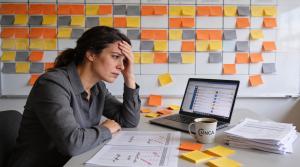A female conference planner in her 30s looks stressed and unhappy as she's surrounded by a sticky notes trying to plan her conference speaking sessions
