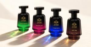 Four Nasmah perfume bottles with green, pink, blue and amber glass, casting long shadows and colored reflections on a cream surface.