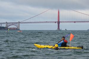 A woman with a yellow swim cap is swimming next to a man in a yellow kayak in the San Francisco bay.