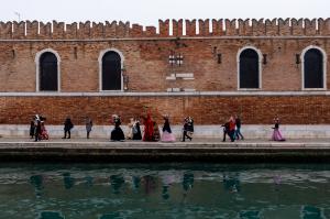 Costumed revellers walk beside the walls of the Arsenale during Carnival in Venice, Italy, photographed on a Fernwayer photography experience. Photo: Fernwayer