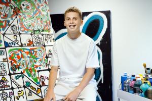 Joe Whale artist sitting with his work