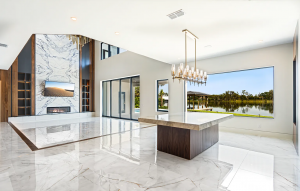 Open living area with polished stone floors, book-matched marble fireplace wall, wood-based island and lake-view window