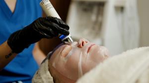 Skincare professional using a Glacē™ LED handpiece over a biocellulose facial mask during a Glacē facial treatment at Indigo the Salon in Jefferson City, MO