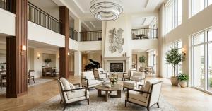 Contemporary senior living lobby with a double height atrium, fireplace, cream lounge seating, wood columns and abundant natural light.