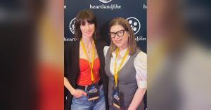 Devin Sidell and Amy Byer Shainman smiling in front of a Heartland Film backdrop, both wearing Heartland International Film Festival filmmaker badges.