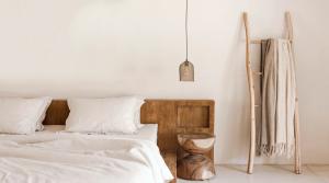 Natural linen bedding on a low wooden bed beside a ladder draped with linen throws