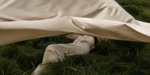 A person resting in long grass beneath a drifting natural fibre sheet