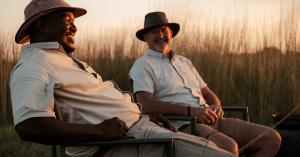 Two men sitting together with a sunset backdrop, smiling.