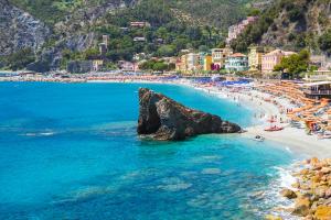 view of the sandy beach of monterosso in summer 2026 with clear water, people bathing and colored umbrellas
