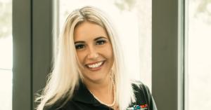 Victoria Litteral smiling in a branded Your Home Sold Guaranteed Realty Exclusive polo shirt beside a sunlit window