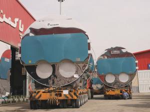 Two large Packman boilers on heavy-haul trailers outside a red factory building, with Packman branding visible.