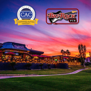 Big Rock Pub resort complex glowing at sunset, with landscaped lawn, winding path, palm trees, mountains, and colorful sky.