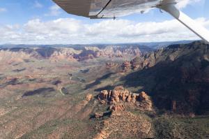 View from plane showing red rock mountains and a winding road that sits between a mountainous valley