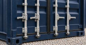 Close-up of the four locking bars, cam handles, rubber door gasket and corner castings on the closed doors of a navy-blue steel shipping container