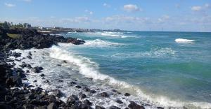 Powerful white capped waves rolling in towards the shore over black volcanic rock of the Aewol coastline, Jeju Island