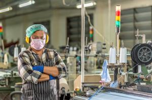 Worker stands with arms folded in front of machinery within a textile manufacturing facility