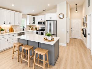 Bright modern Florida home kitchen featuring white cabinetry, stainless steel appliances, a spacious kitchen island, and wood flooring – Joe Tumolo Realtor.