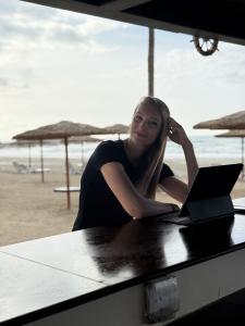 blonde woman sat by the beach with laptop in hand