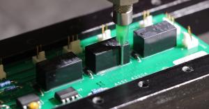 Dymax adhesive being dispensed around a component to secure it to a printed circuit board.