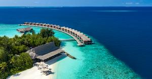 Aerial view of Grand Park Kodhipparu Maldives showing a curved row of overwater Reef Pool Villas, turquoise lagoon waters, the surrounding house reef and a beachfront restaurant in North Malé Atoll.